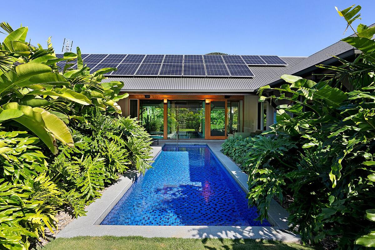A modern house with a swimming pool, surrounded by lush greenery, and solar panels on the roof.