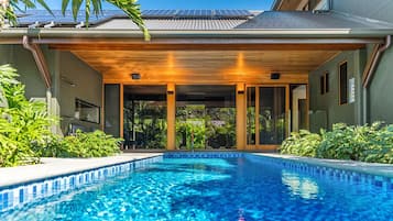 Relax by the rectangular pool surrounded by lush greenery and a shaded pergola.