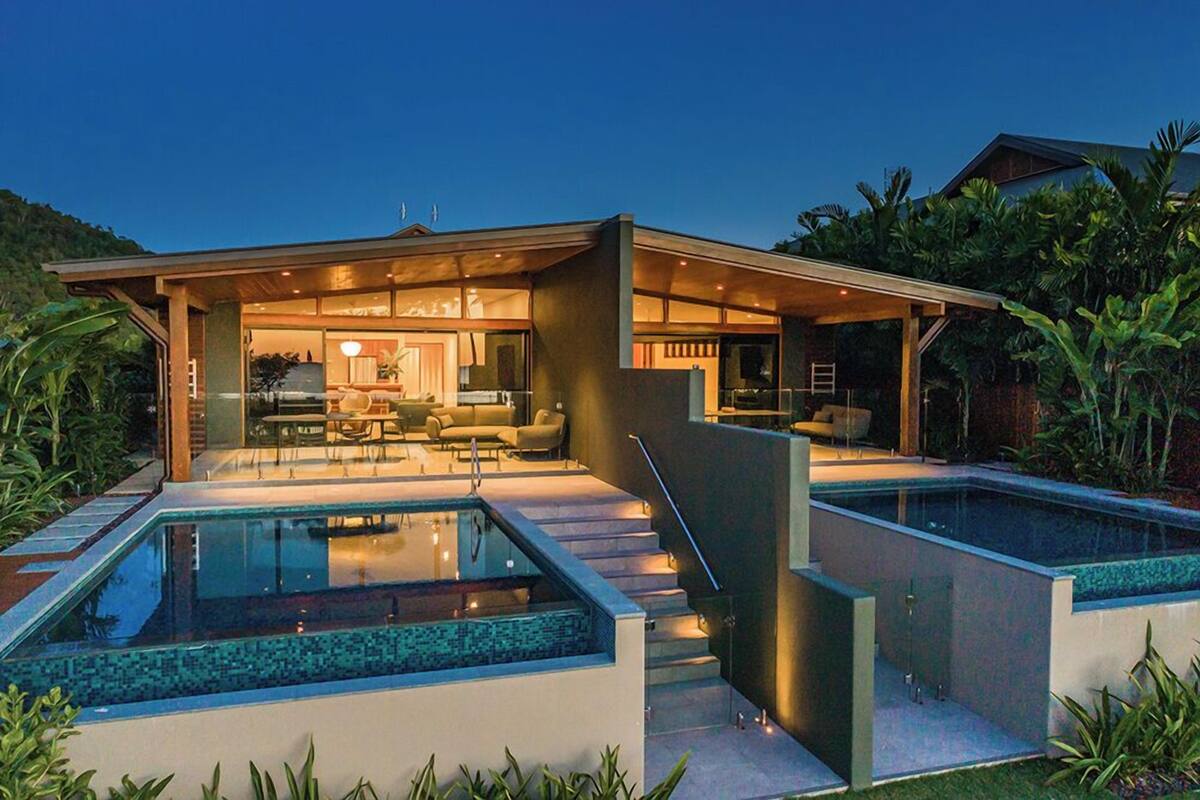 A modern house with a glass-enclosed pool, a covered outdoor seating area, and a staircase leading to a second level.