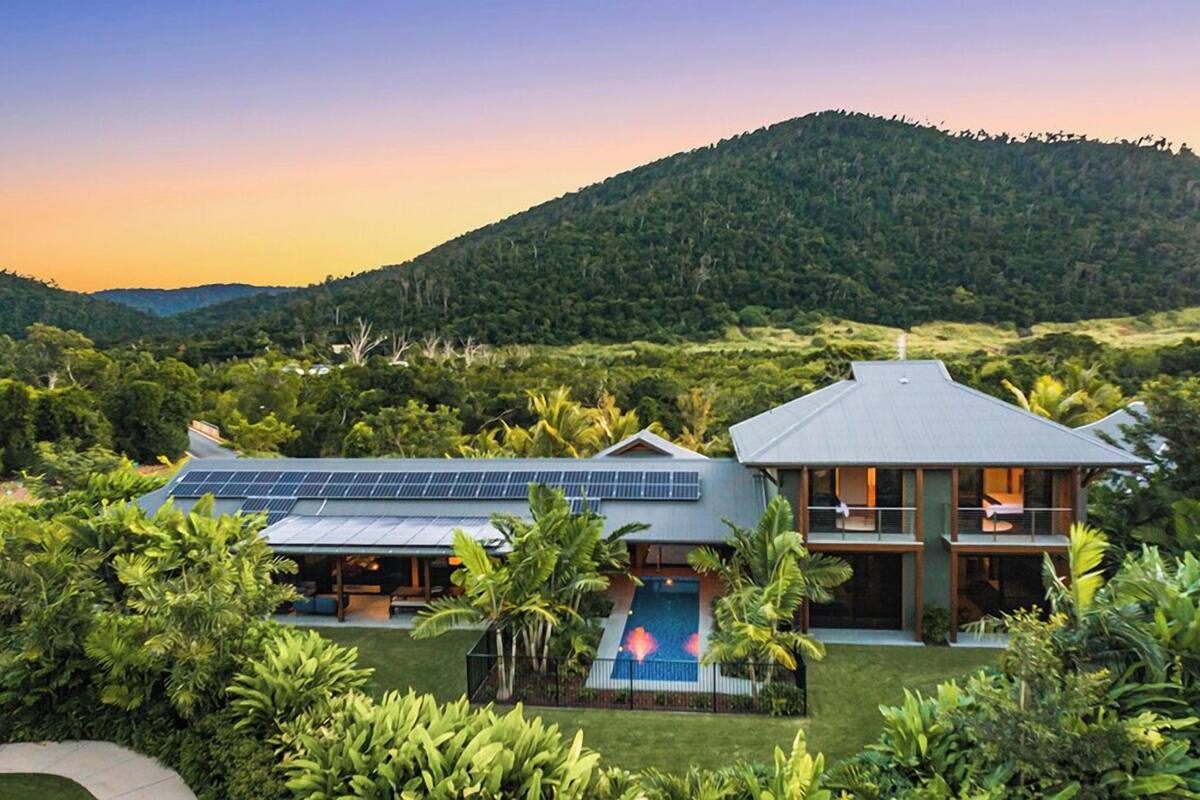 A modern house with a swimming pool, surrounded by lush greenery and a hilly landscape.