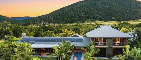 A modern house with a swimming pool, surrounded by lush greenery and a hilly landscape.
