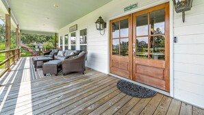 Een overdekt terras met houten vloer, rieten meubels en een houten deur met ruitpanelen.