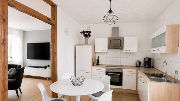 A modern kitchen with white cabinets, a built-in oven, and a dining area with a round table and chairs.