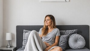 A person sitting on a bed with a grey blanket, grey pillows, and a grey headboard.