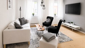 A modern living room with a white sofa, a black armchair, a coffee table, and a TV mounted on the wall.