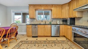 Una cucina con mobili in legno, elettrodomestici in acciaio inossidabile, un tavolo da pranzo con sedie e un tappeto decorato.