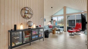 A spacious living room with a wooden floor, a glass cabinet with board games, a globe, and a red chair. - 3 bedroom beautiful home in Aakirkeby (Aakirkeby)