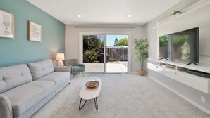 A modern living room with a sofa, a coffee table, a TV, and a sliding glass door leading to an outdoor area. - Beautiful, Stylish 3 Bedroom Home in San Jose! (San Jose)