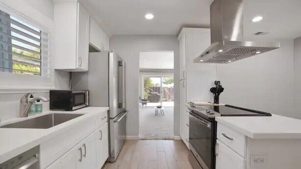 A modern kitchen with white cabinetry, a stainless steel range hood, and a microwave. - Beautiful, Stylish 3 Bedroom Home in San Jose! (San Jose)