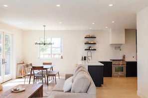 Una cocina moderna con una isla central, un comedor con mesa y sillas, y una sala de estar con sofá.