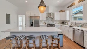 A modern kitchen with a large island, bar stools, and a hanging light fixture. - Updated and Spacious 3BR/2BA Victorian Style Home (Petaluma)