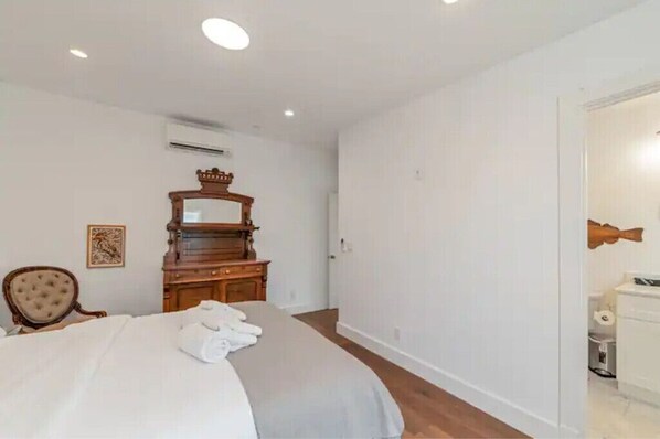 A bedroom with a bed, a wooden dresser, a mirror, a chair, and a small bathroom visible through an open door. - Updated and Spacious 3BR/2BA Victorian Style Home (Petaluma)