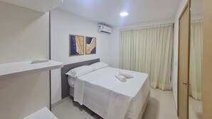 Een hotelkamer met een bed, nachtkastje, een luchtverkoeler aan de muur en een raam met gordijnen.