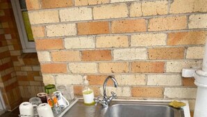 A small white kitchen area with a sink, a tray with kitchen items, and a cabinet with drawers.