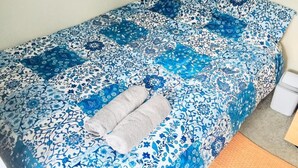 A bed with a blue floral bedspread and two pillows. A towel is placed on the bed.