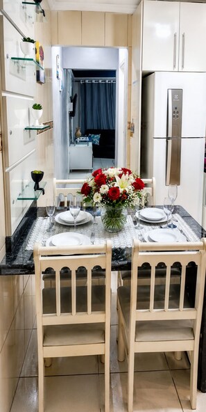 A dining area with a table set for two, a refrigerator, and a kitchen counter. - Beautiful house with a swimming pool heated by solar power year-round, near the beach. (Praia Grande)