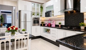 A modern kitchen with white cabinetry, a black countertop, and stainless steel appliances. - Beautiful house with a swimming pool heated by solar power year-round, near the beach. (Praia Grande)