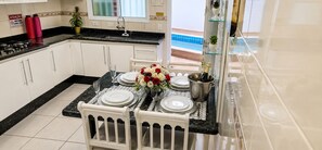 A kitchen with a dining area set for a meal, a sink, and a view of a pool.