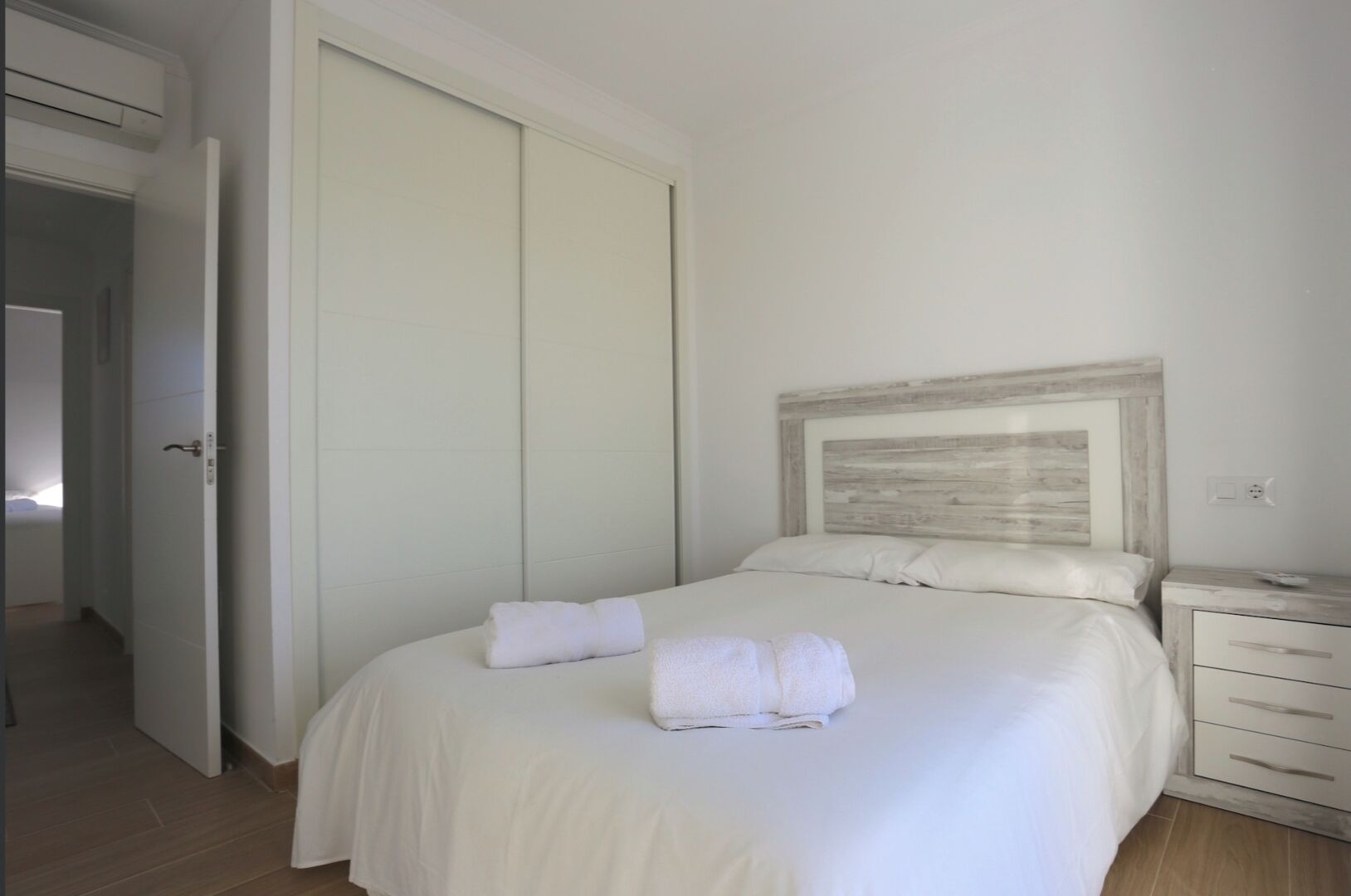 Een slaapkamer met een groot bed, een houten hoofdbord, een nachtkastje en een gesloten deur.