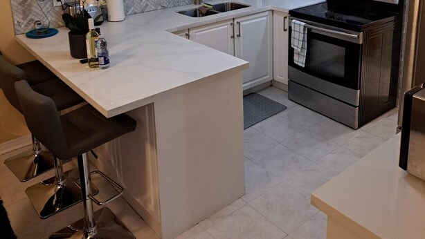 A modern kitchen with white cabinets, a stainless steel stove, and a herringbone-patterned backsplash. - Luxury getaway (Brampton)