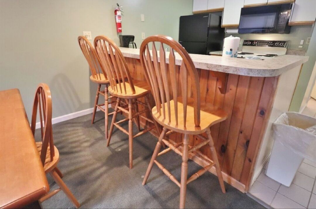 A kitchen with wooden chairs, a counter, a microwave, and a fire extinguisher.