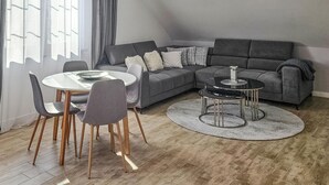 Un soggiorno moderno con un divano angolare grigio, un tavolo da pranzo rotondo con sedie e due tavolini.