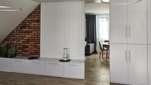 Una cucina moderna con mobili bianchi, un muro a mattoni e un'area pranzo sullo sfondo.