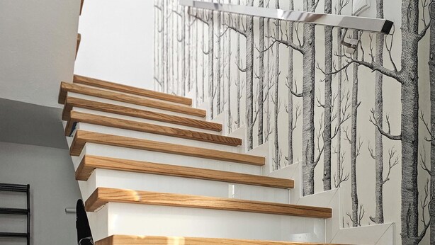 Una scala con ringhiere in legno e un muro decorato con un motivo arboreo.