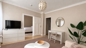 A modern living room with a flat-screen TV, a white desk, a comfortable sofa, and a large plant.