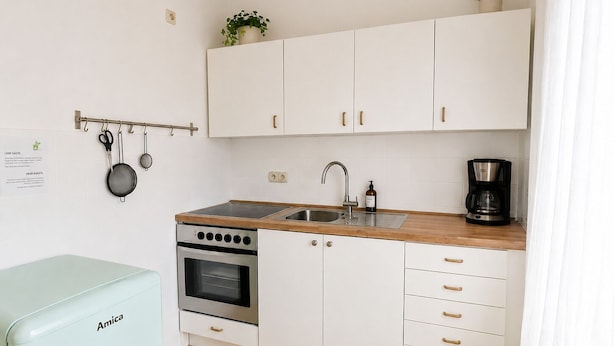 A compact kitchenette with white cabinets, a built-in oven, a sink, and a coffee maker.