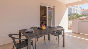 Un coin repas avec une table et des chaises, une fenêtre donnant sur des immeubles et une porte menant à la cuisine.