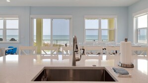 Una cocina moderna con un lavamanos de acero inoxidable, encimeras blancas y grandes ventanas con vistas al océano.