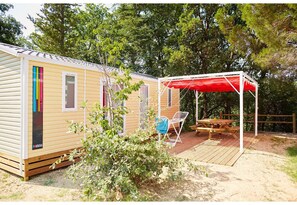 A mobile home with a covered patio area, a small deck, and a chair. - Proche d'Argelès | Parc Aquatique | Camping 4* (Laroque des Albères)