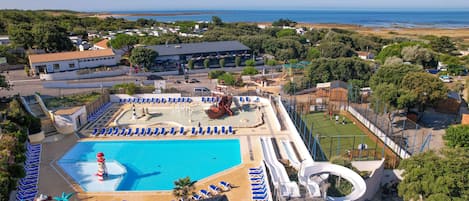 A resort with a large swimming pool, sun loungers, a water slide, and a view of the sea.