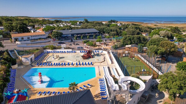 Ein Resort mit großem Schwimmbecken, Liegestühlen, einer Rutsche und Blick auf das Meer.