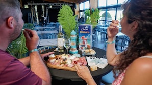 Una mesa de comedor con una variedad de quesos, aceitunas y pan, acompañada de copas y botellas de vino.