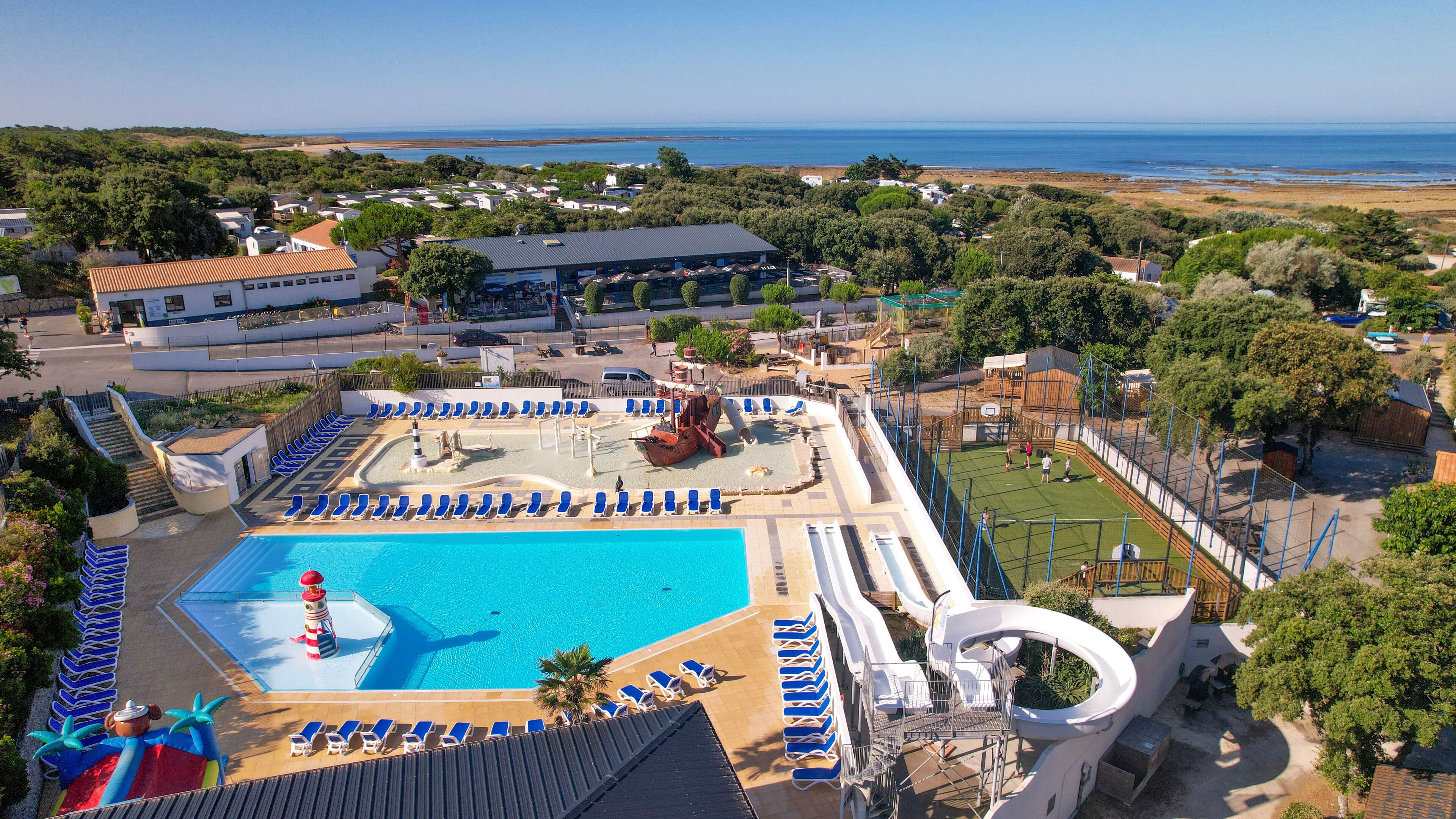 A resort with a large swimming pool, sun loungers, a water slide, and a view of the sea.