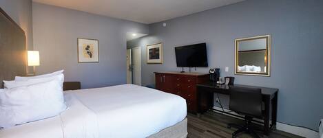A hotel room with a large bed, a desk, a television, and a mirror.