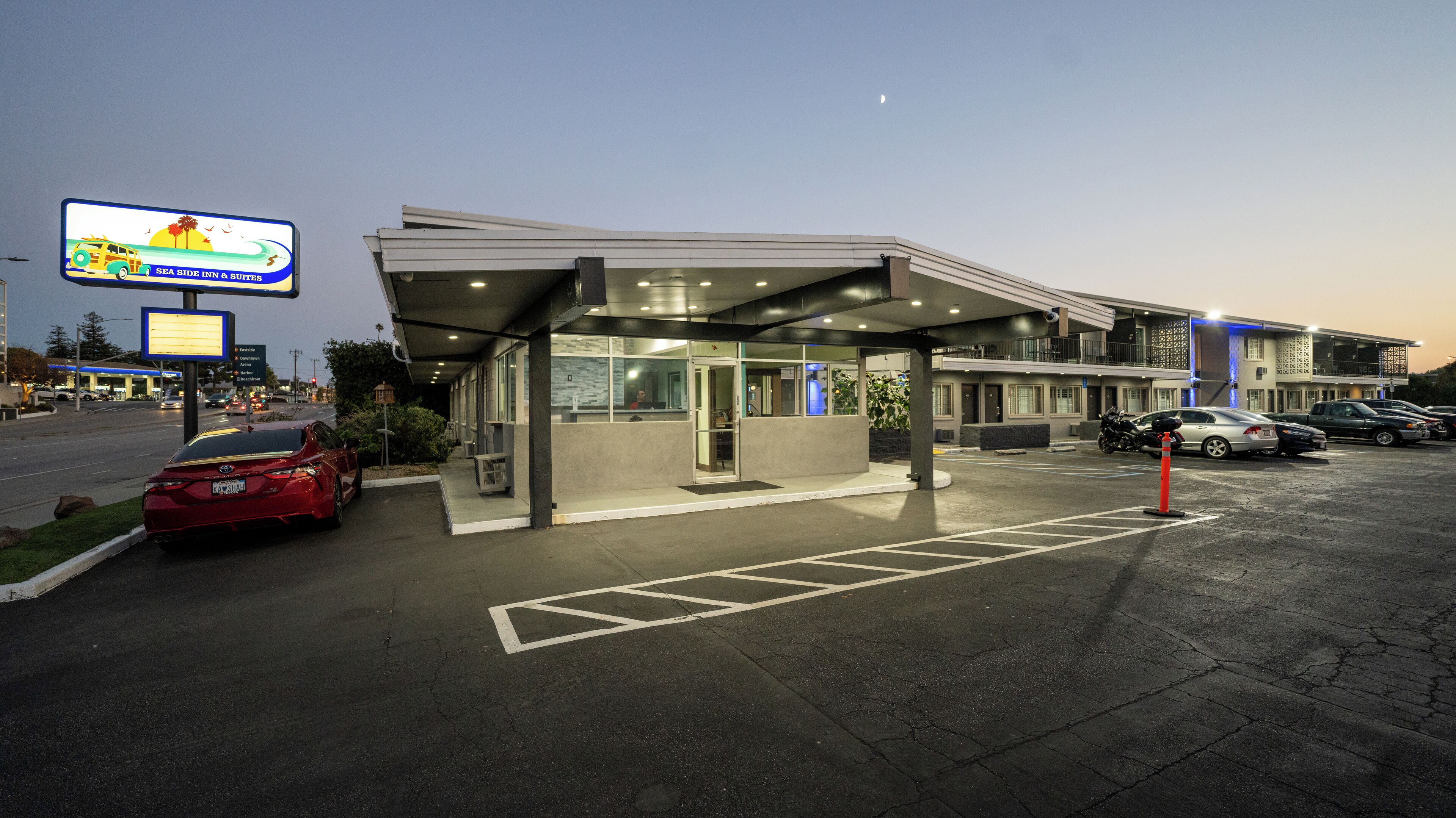A hotel with a covered entrance, a parking lot, and a signboard advertising a nearby establishment.