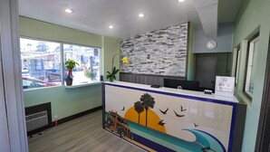 A reception desk with a modern design, a large window offering a view of the street, and a decorative mural on the wall. - Seaside Inn & Suites (Santa Cruz)