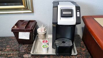 Eine Kaffeemaschine mit dem Aufkleber Hamilton Beach, ein Mülleimer und ein Tablett mit zwei Tassen Kaffee und einem Zuckergefäß.