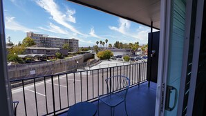 A balcony with a view of a parking lot, a building with multiple floors, and palm trees. - Seaside Inn & Suites (Santa Cruz)