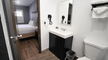 Una camera d'albergo con un letto, un lavandino bianco, uno specchio e un water.