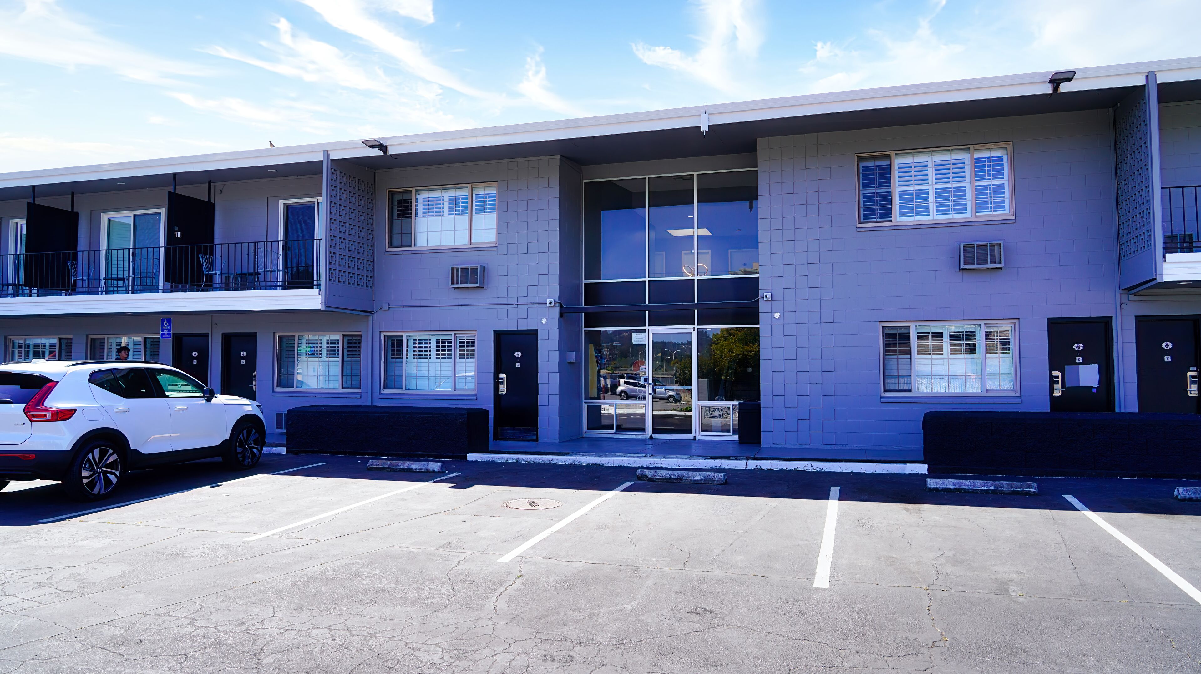 A modern building with a parking lot, large windows, and a white car parked in front.