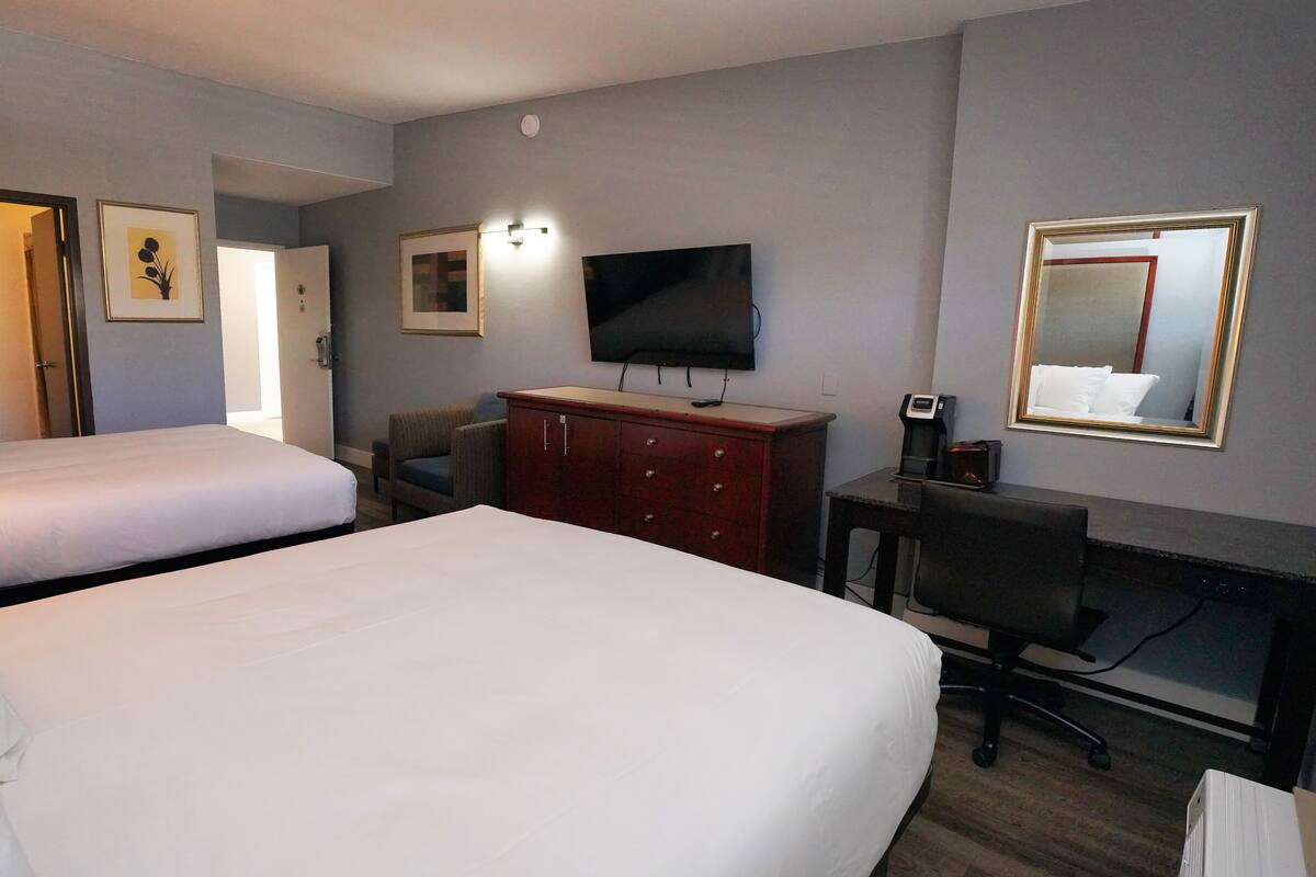 A hotel room with two beds, a TV, a desk with a chair, a dresser, and a mirror.