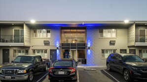 A multi-story building with a modern design, featuring a central entrance with glass doors, parking spaces on either side, and a blue-lit facade. - Seaside Inn & Suites (Santa Cruz)