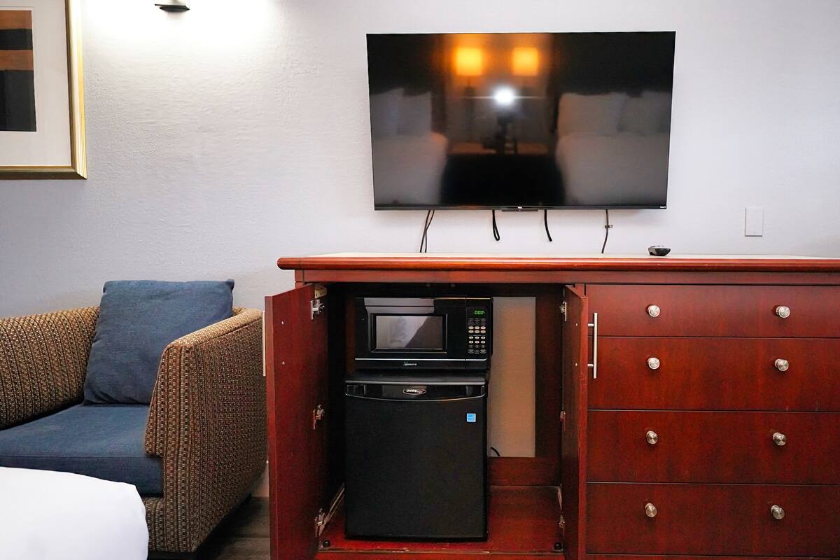 A compact kitchenette with a microwave, a coffee maker, and a small refrigerator. A flat-screen TV is mounted on the wall above the kitchenette.