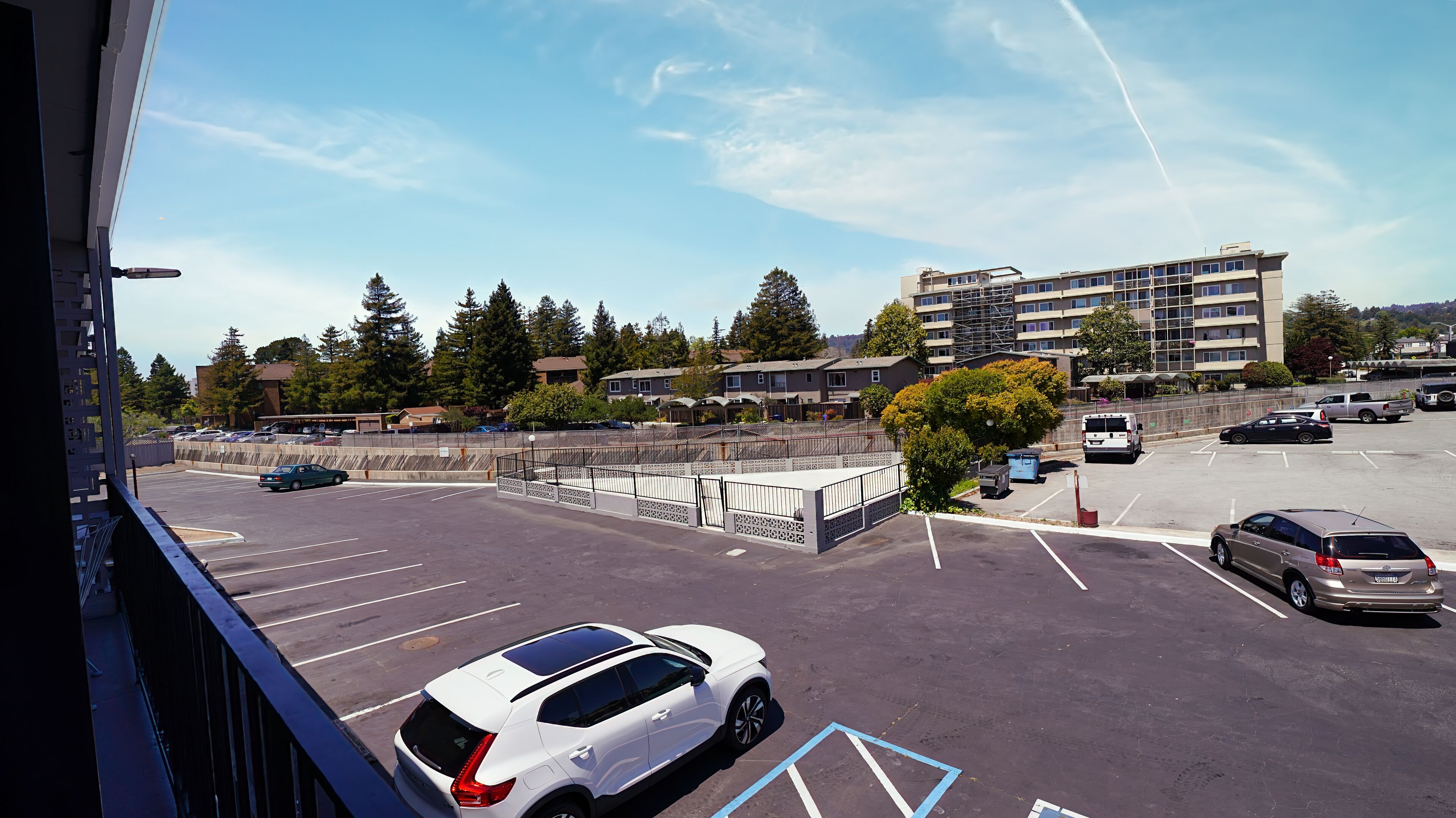 A parking lot with multiple cars, a white SUV in the foreground, and a multi-story building in the background.