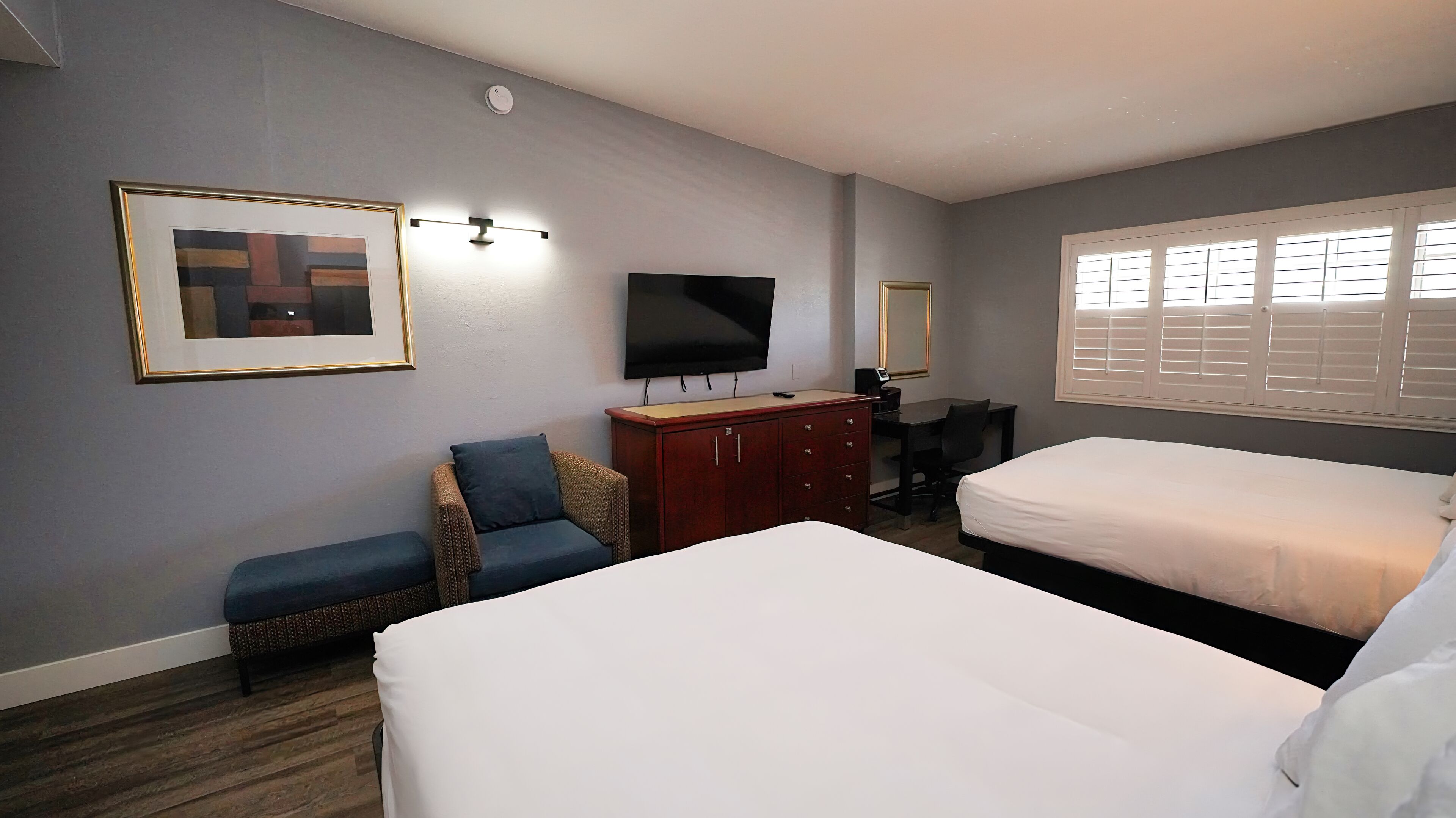 Habitación de hotel con dos camas, un escritorio, una silla, un televisor y un cuadro en la pared.