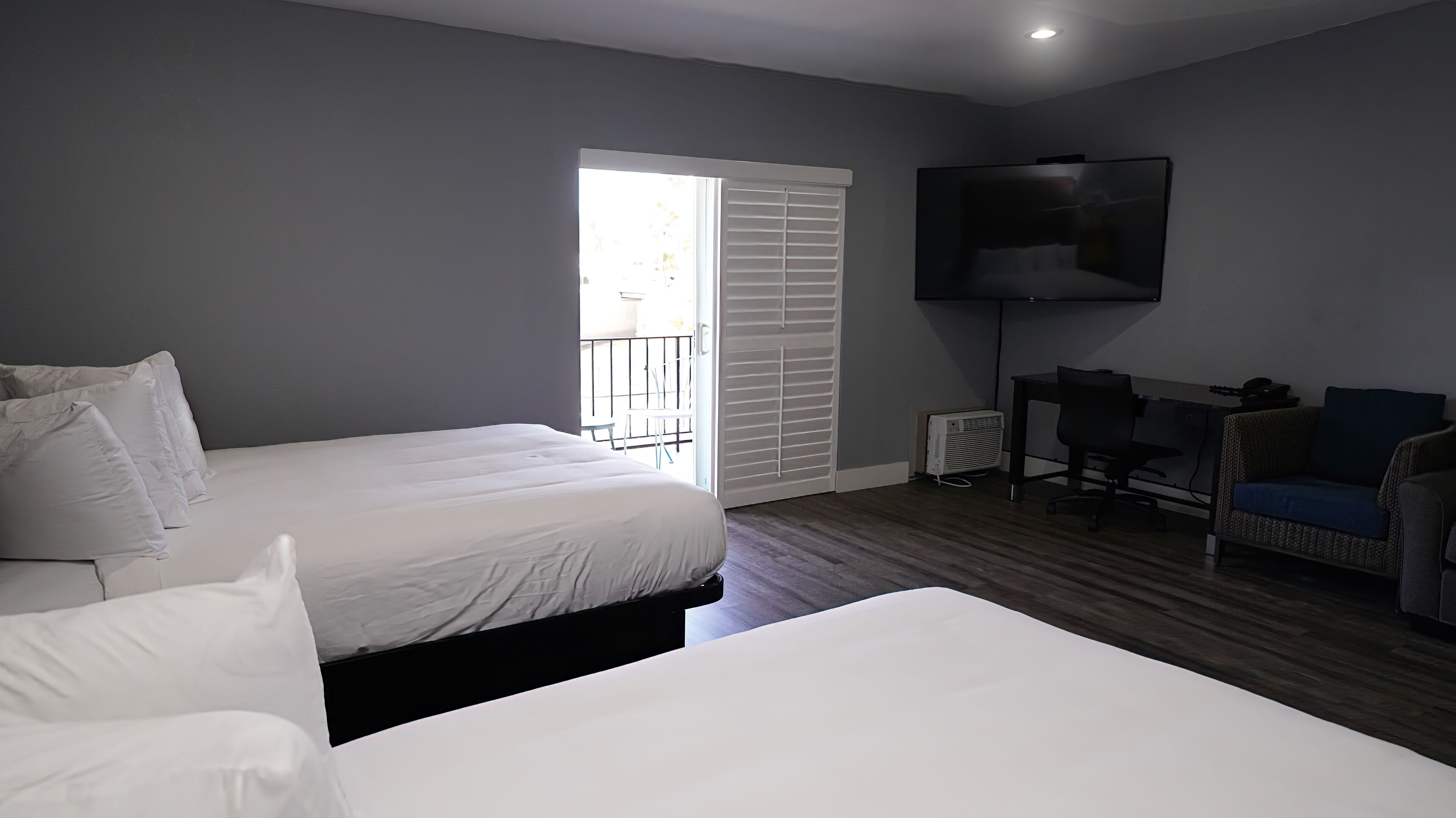 Une chambre avec deux lits, un bureau, une chaise, un téléviseur et une fenêtre avec des stores.